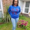 Ankara “LOVE Africa” Sweatshirt – Royal Blue | Leopard Print Appliqué Woman wearing a royal blue sweatshirt with pink and black Ankara leopard print appliqué spelling ‘LOVE’ with Africa-shaped ‘O’, standing in a garden.