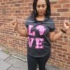 Hooded t-shirt with a curved hem Woman wearing a black hooded t-shirt with a curved hem, featuring bold pink Ankara appliqué “LOVE” lettering on the front.