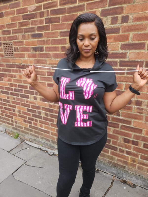 Hooded t-shirt with a curved hem Woman wearing a black hooded t-shirt with a curved hem, featuring bold pink Ankara appliqué “LOVE” lettering on the front.