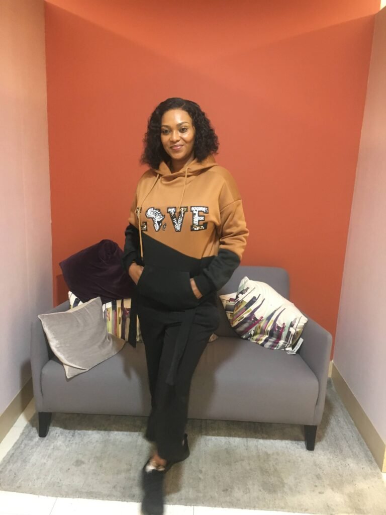 Woman wearing a brown and black colour block hoodie with bold varsity-style “LOVE” Ankara appliqué design.