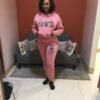 Woman wearing a pink hoodie and jogger set with bold Ankara appliqué “LOVE” design on the chest and thigh.