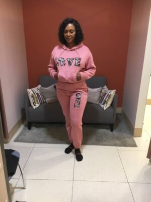 Woman wearing a pink hoodie and jogger set with bold Ankara appliqué “LOVE” design on the chest and thigh.
